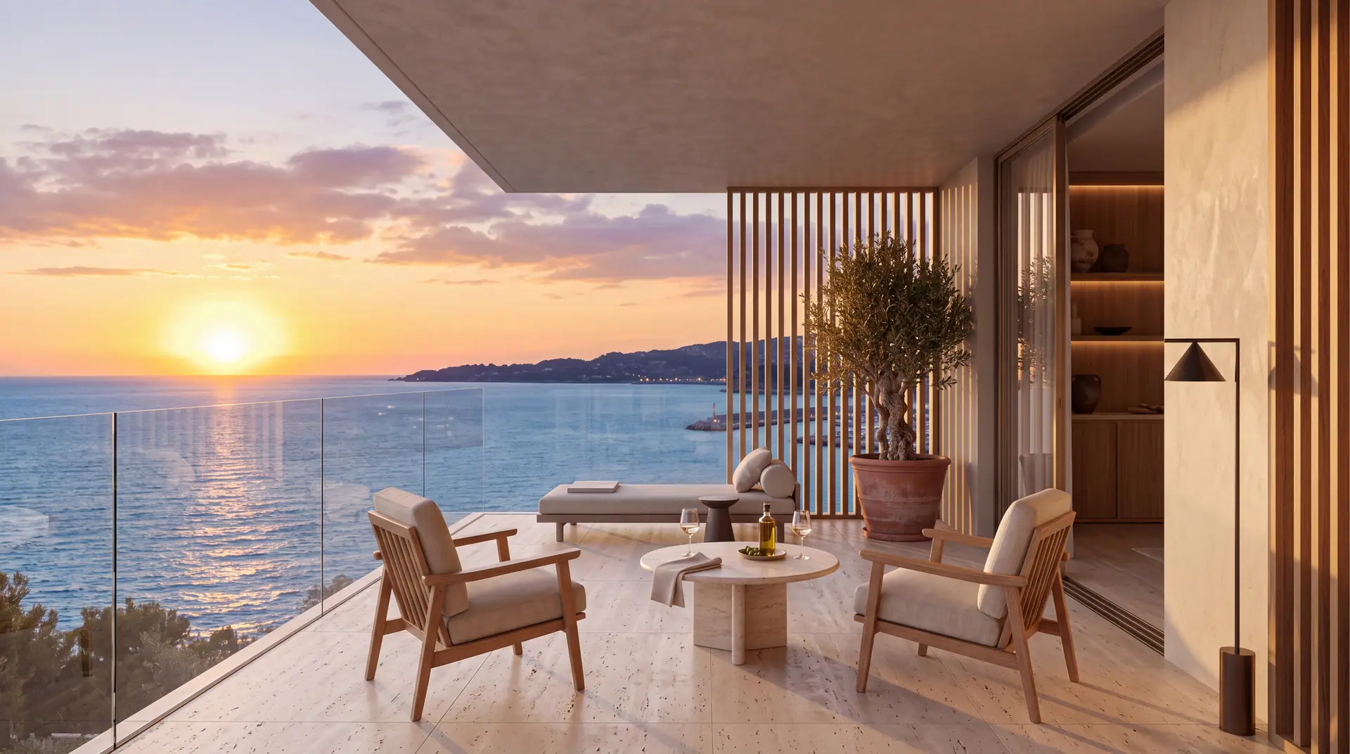 Balcony with two armchairs and a small table behind a glass balustrade, the sun setting over the sea